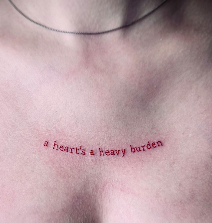 A small tattoo idea featuring the quote "a heart's a heavy burden" in delicate red ink, symbolizing resilience and emotional strength.