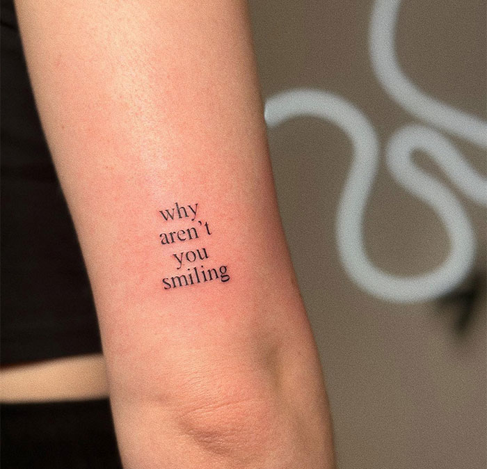 A small tattoo idea featuring the phrase "why aren't you smiling" in minimalist black ink, conveying a thought-provoking message about joy and introspection.