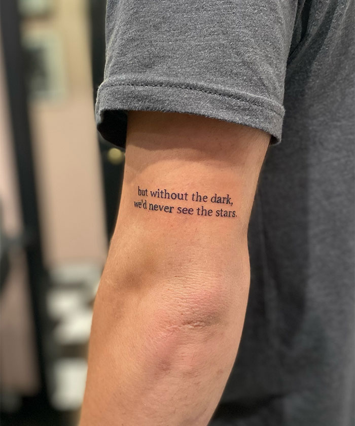 A small tattoo idea featuring the phrase "but without the dark, we’d never see the stars" in a minimalist black font along the inner arm, symbolizing resilience and finding light in tough times.