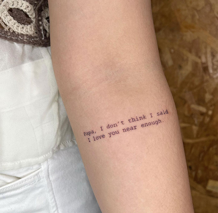 A small tattoo idea featuring the heartfelt phrase, "Papa, I don't think I said I love you near enough," in a simple, typewriter-style font on the inner arm, creating a personal tribute to a loved one.