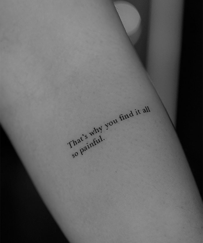 A small tattoo idea featuring the phrase, "That's why you find it all so painful," in a delicate, italicized font on the forearm, capturing a sense of vulnerability and introspection.