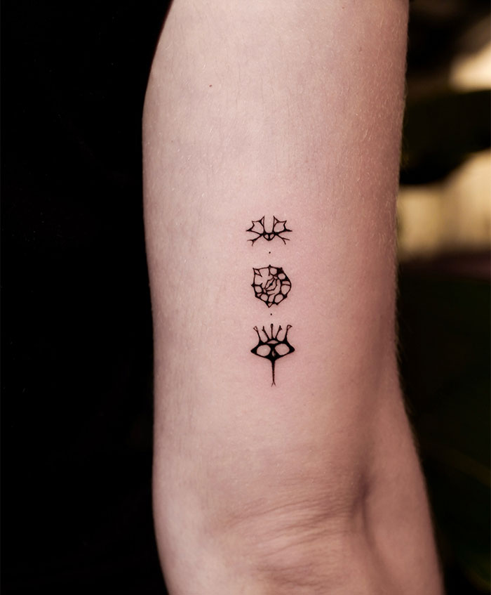 "A small tattoo idea featuring three abstract symbols in a vertical line on the forearm, creating a unique and mystical design."