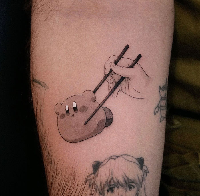 A small tattoo of Kirby being picked up with chopsticks, blending a cute character with playful imagery.