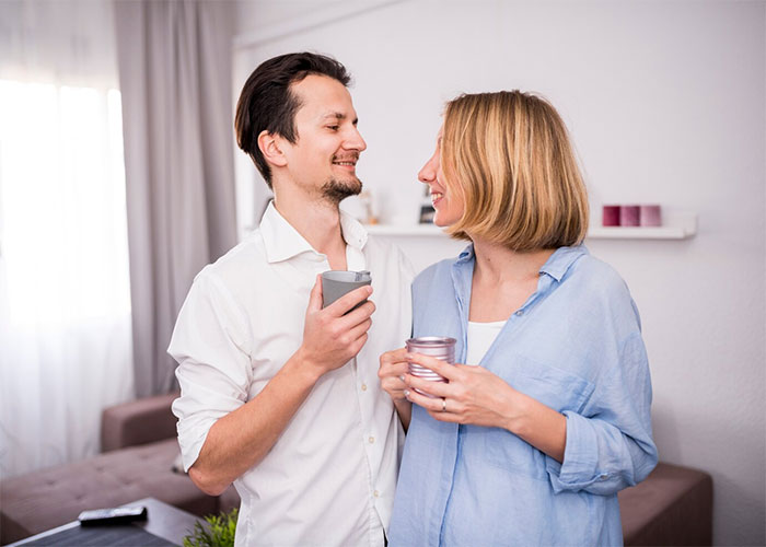 Couple smiling at each other, holding drinks in a cozy living room setting, discussing family plans.