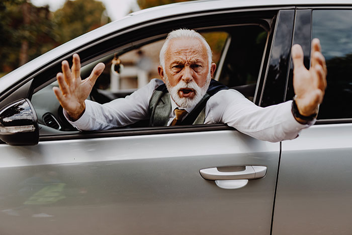 Elderly man angrily gesturing from car window, highlighting sexism issue.