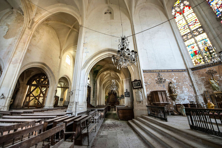 Abandoned sacred place in Europe with high arches, stained glass windows, and wooden pews.