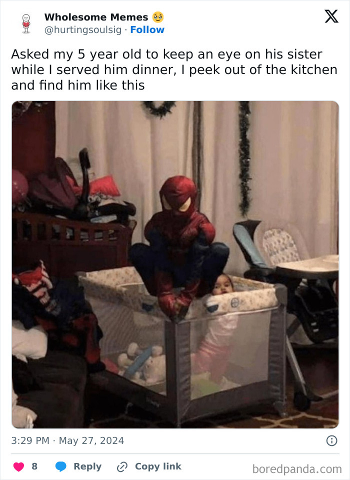 Child dressed as Spider-Man crouches on playpen in a room, with a younger sibling inside, embodying spot-on humor in parenting.