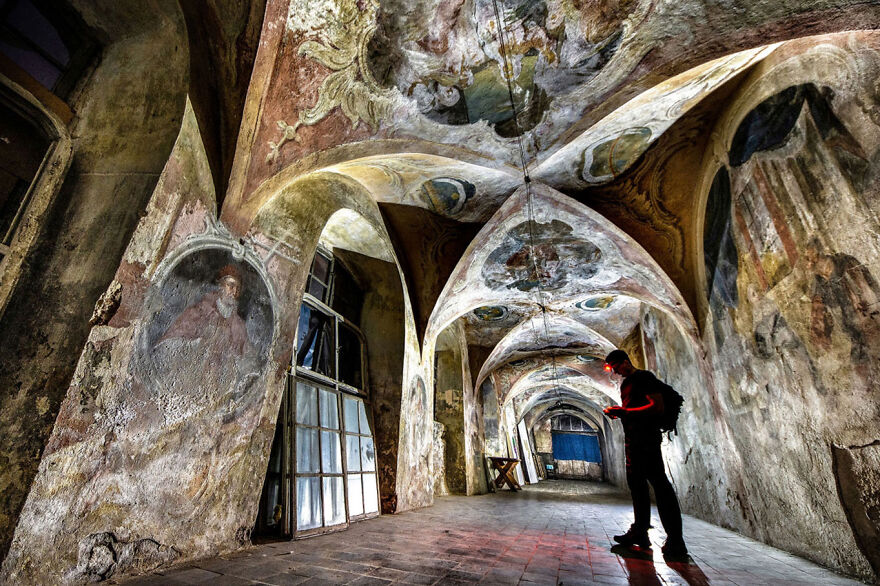 Person exploring beautiful abandoned sacred place in Europe with frescoed ceilings and arched corridors.