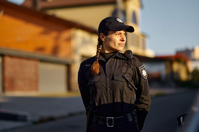 A confident female police officer stands in uniform outdoors, representing resilience against sexism.