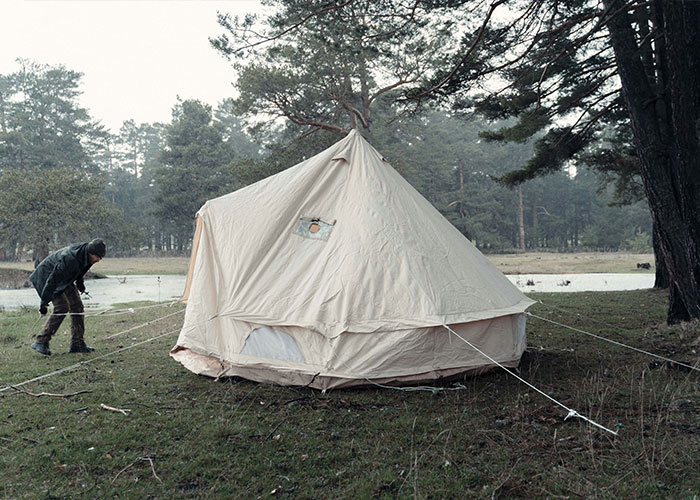 A person secures a large tent in a forest clearing, illustrating interesting facts from the “Today I Learned” community.