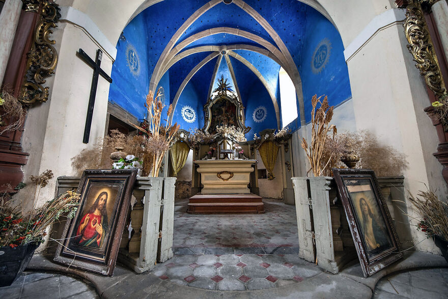 Abandoned sacred place in Europe featuring an altar, blue vaulted ceiling, and religious paintings.