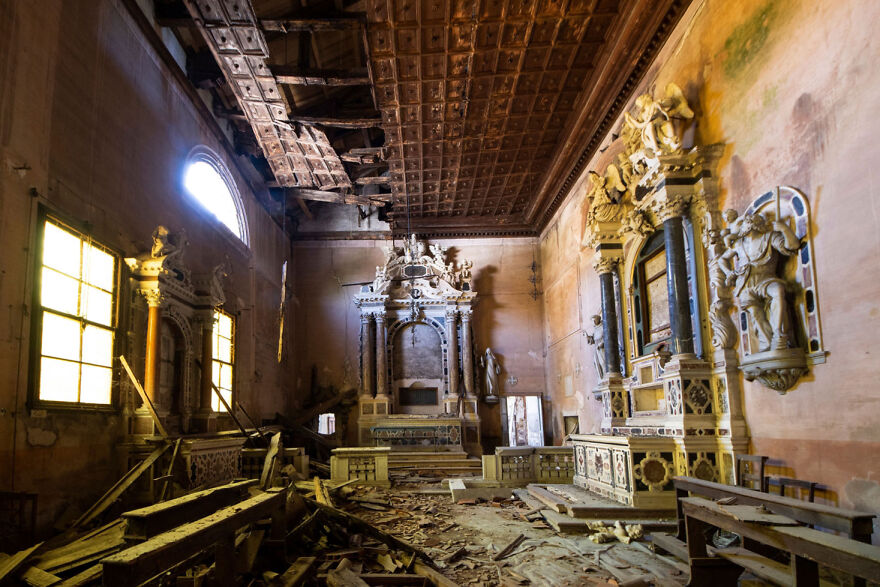 Abandoned sacred place in Europe with ornate altar, decaying wooden benches, and sunlight through a large window.