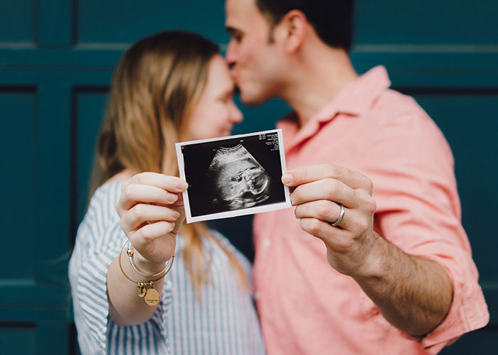 Couple holding an ultrasound photo, with the man kissing the woman's forehead, symbolizing future parenting challenges.