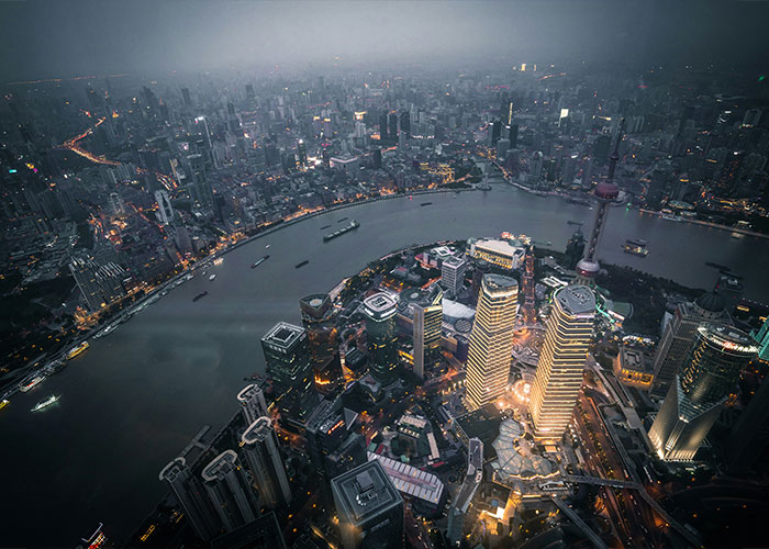 Aerial view of a city skyline at night, lights illuminating buildings along a winding river, showcasing urban architecture.