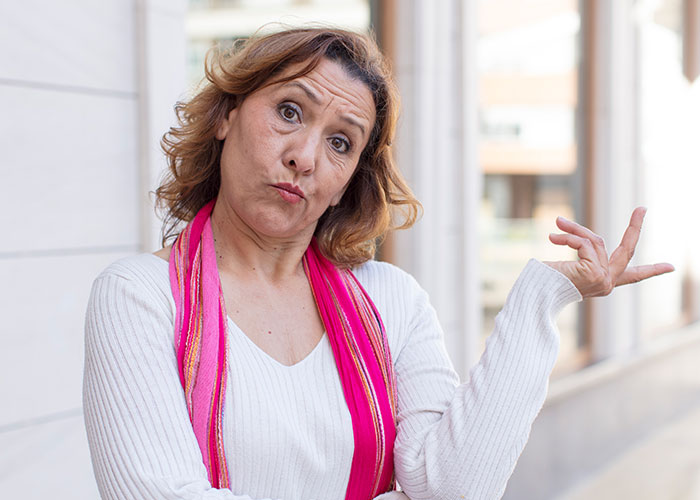 Neighbor woman in white sweater and pink scarf making a dismissive gesture outside.