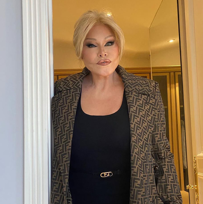 Jocelyn Wildenstein in designer outfit, standing in a doorway.