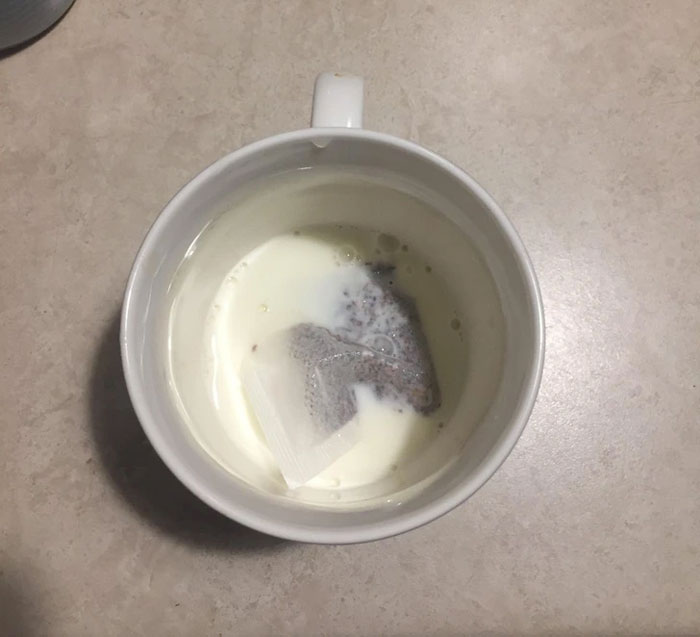 Teabag submerged in a cup of milk on a countertop, illustrating a frustrating boyfriend's act.