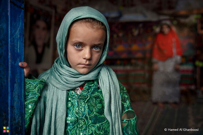 Young girl in a green patterned dress and headscarf stands in focus, highlighting sustainability themes in breathtaking photography.