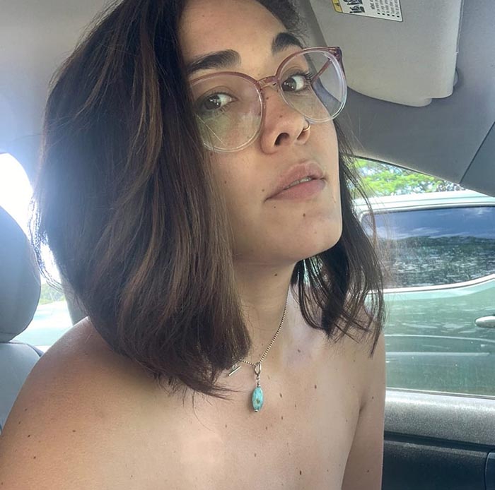 Hannah Kobayashi sitting in a car, wearing glasses and a turquoise necklace; related to missing person and airport investigations.