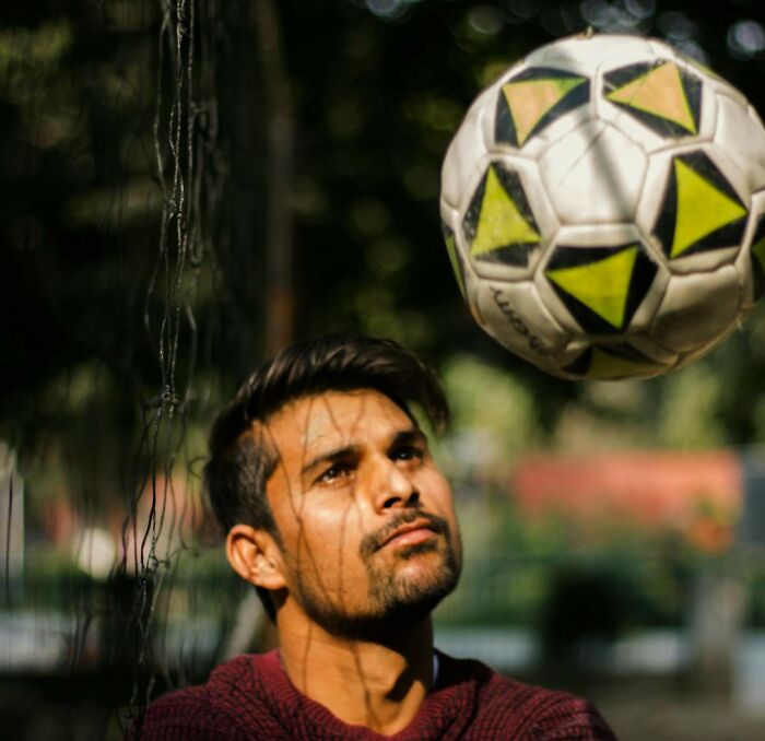 Man looking at a soccer ball with a thoughtful expression, outdoors.