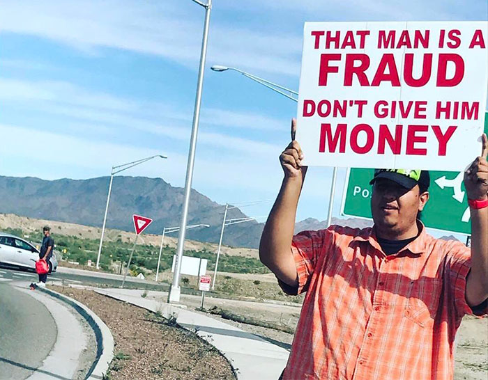 Man holding a sign about fraud on a roadside, reflecting the 'Choosing Beggars' reality check theme.