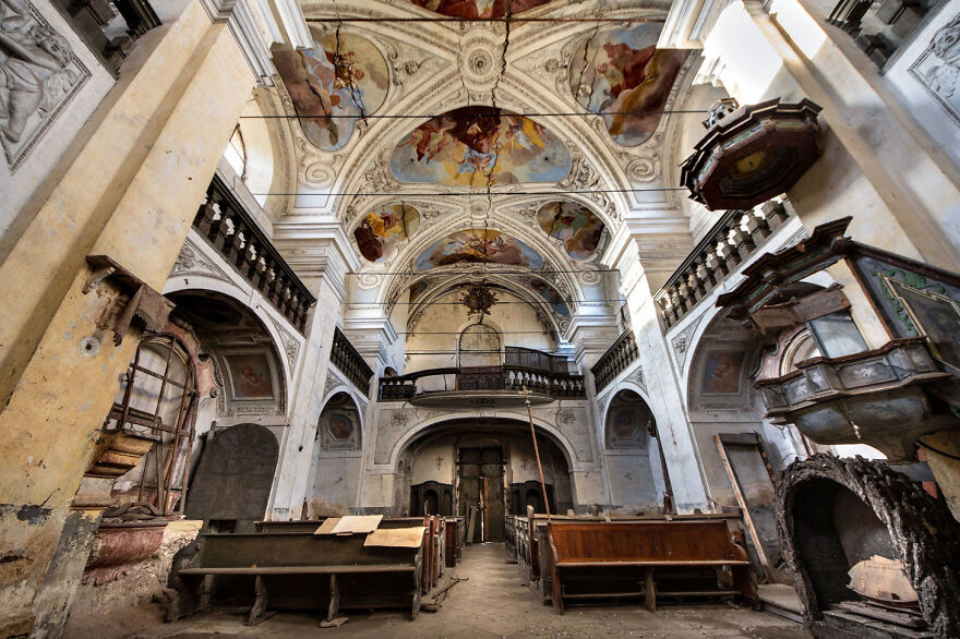 Abandoned sacred place in Europe featuring a dilapidated interior with ornate ceiling art and decaying pews.