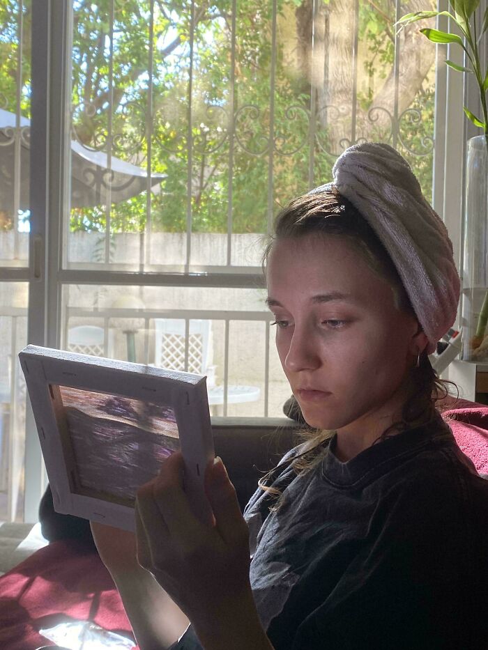 A woman with a towel on her head gazes thoughtfully at a picture, reminiscent of a Renaissance painting.