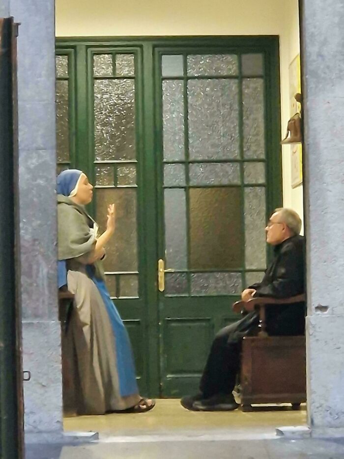 Two people conversing, framed by a doorway, resembling a scene from a Renaissance painting.