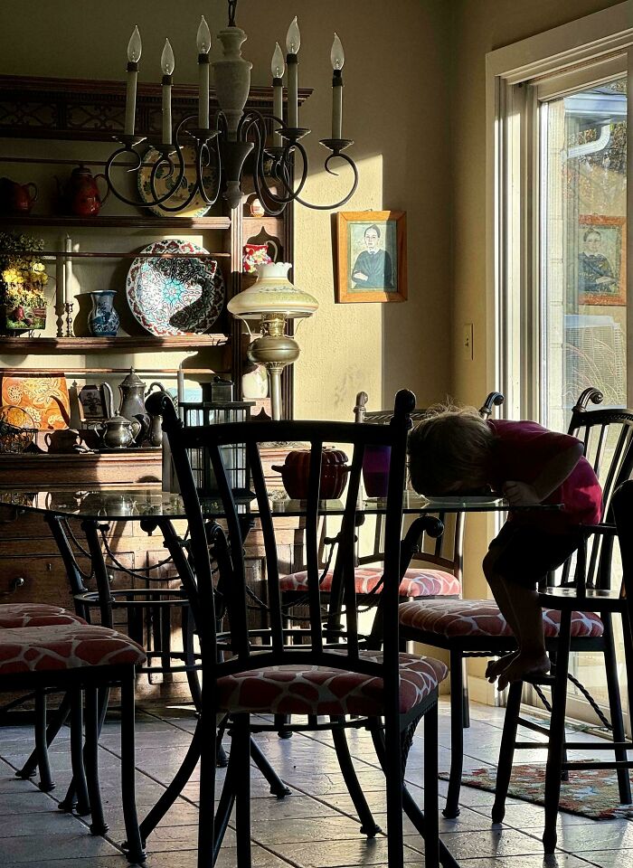 Child in dimly lit dining room, resting head on table, resembling Renaissance painting ambiance.