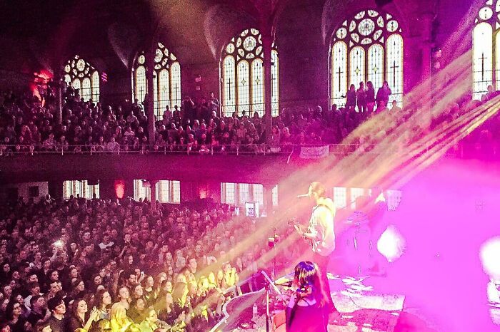 Concert in a repurposed church building conversion, featuring a vibrant audience and colorful lighting effects.