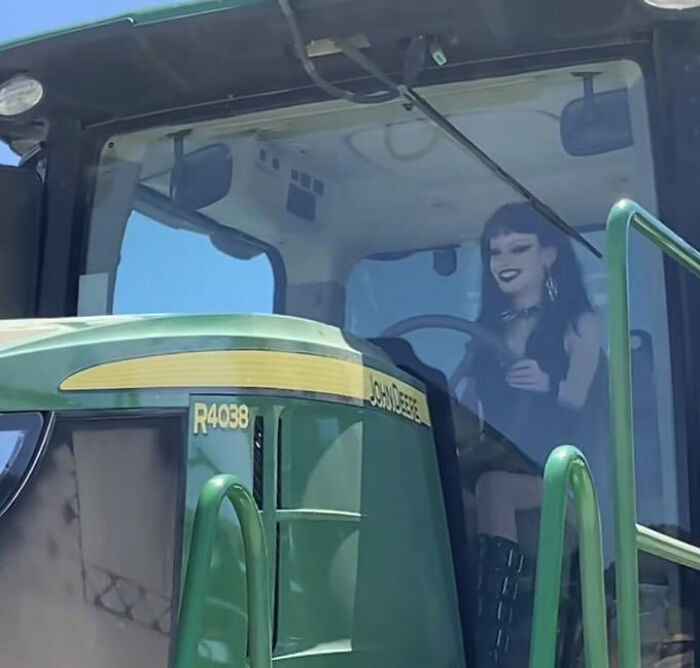 Person dressed uniquely, resembling a "Final Boss," sits in a John Deere tractor cab, creating a striking visual contrast.