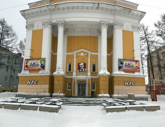 Historic building conversion into a KFC restaurant with neoclassical columns and vibrant yellow façade, snow-covered exterior.