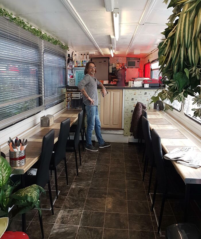 Man inside a unique building conversion cafe, featuring a counter, seating area, and indoor plants.