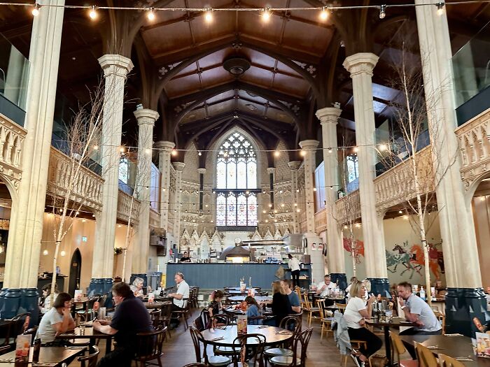 People dining in a converted historic church with high ceilings and stained glass windows, showcasing a unique building conversion.