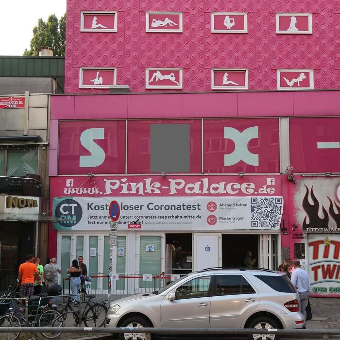 Pink Palace building conversion with silhouette figures on facade, street view with cars and pedestrians.