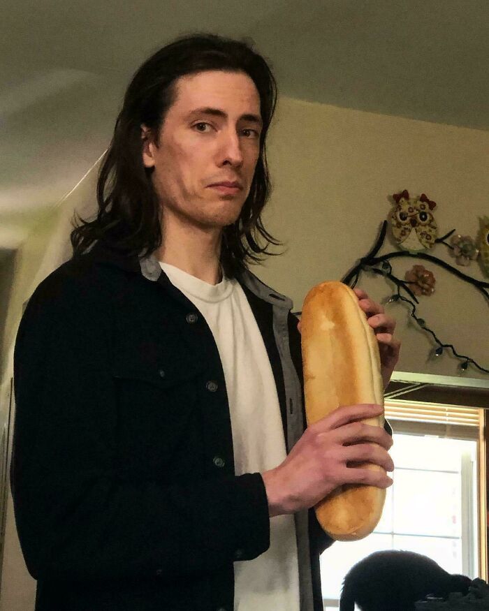 A man holding a baguette, resembling a pose from Renaissance paintings.