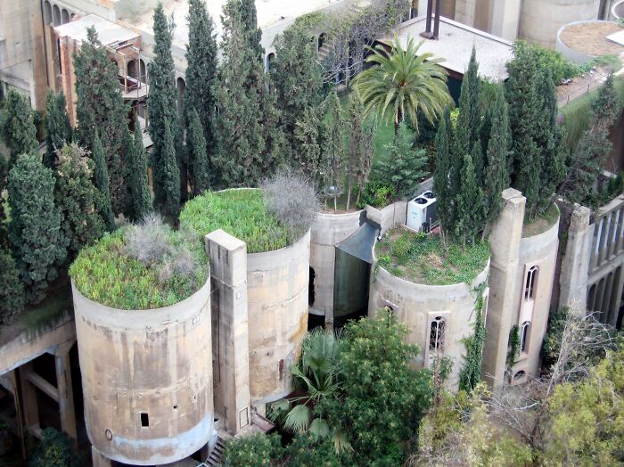 Aerial view of a unique building conversion with cylindrical structures topped with greenery and surrounded by trees.