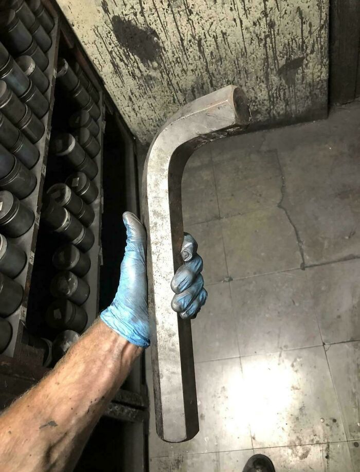 Hand holding an absolute unit of a metal L-shaped tool in a workshop.