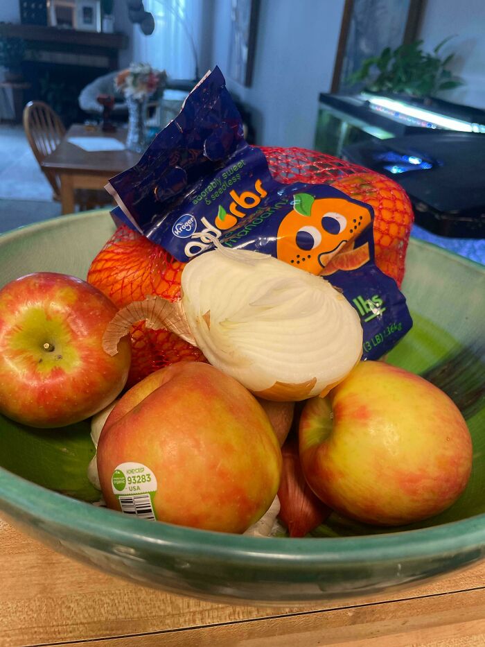 Bowl with apples and an onion mistakenly stored with a bag of oranges, showcasing infuriating boyfriend habits in the kitchen.