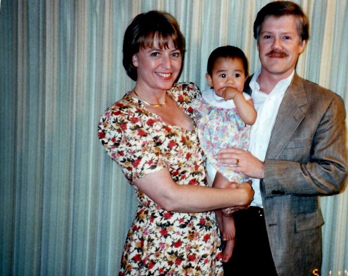 A joyful family portrait showcasing a warm adoption moment, with parents smiling while holding their adopted child.