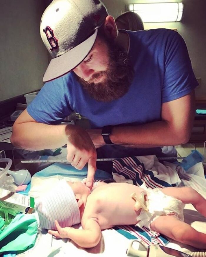 Father gently holding newborn's finger in a hospital, symbolizing a wholesome adoption story moment.