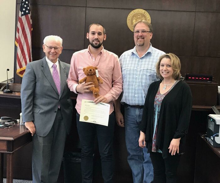 A joyful moment in court with a new family celebrating a wholesome adoption, holding a teddy bear and certificate.