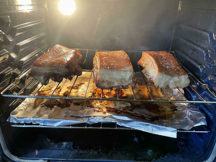 Roasting meat in the oven with fat dripping onto foil, highlighting infuriating kitchen habits of boyfriends and husbands.