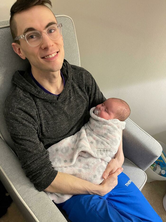 Smiling man in glasses joyfully holds a swaddled baby, showcasing a touching adoption moment.