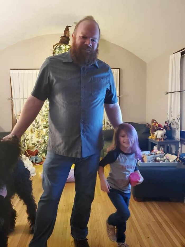 Man and young girl smiling, holding hands in a living room, illustrating a wholesome adoption story.