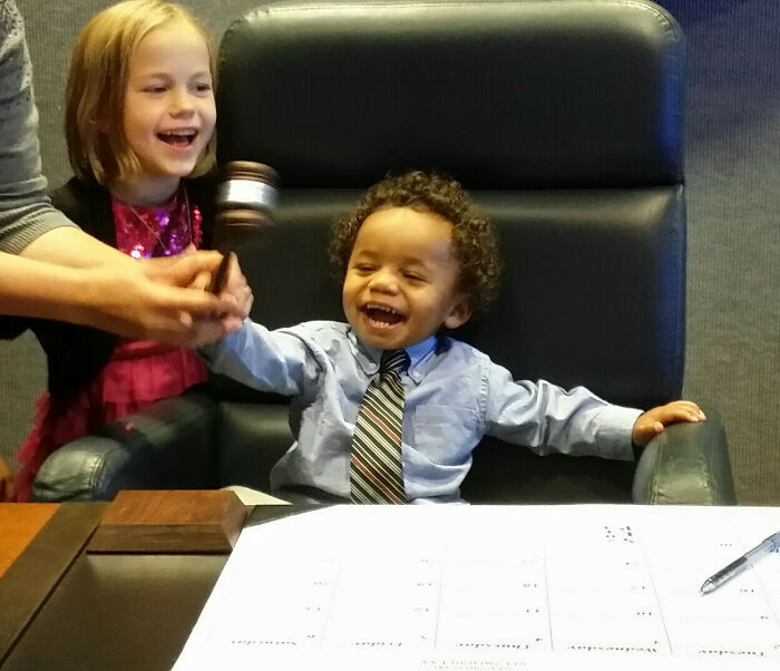 Smiling children in an adoption ceremony moment, holding a gavel.