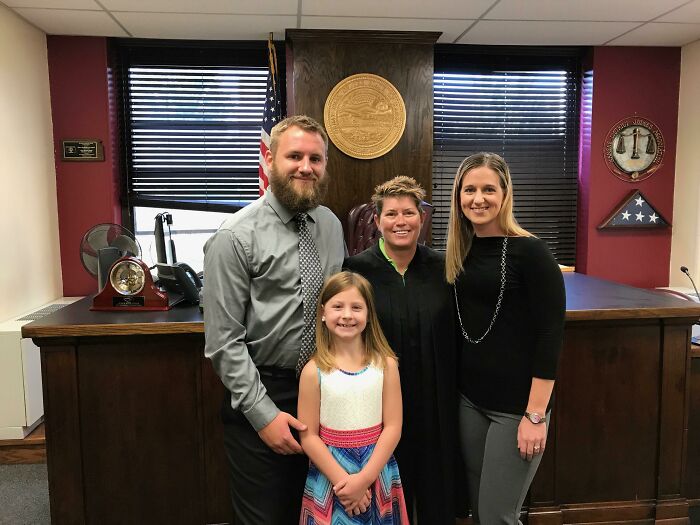 Family celebrating adoption with judge in a courtroom, capturing a heartwarming moment.