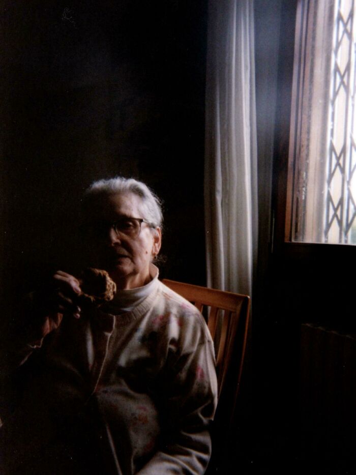 Elderly woman in dim light by window, evoking a Renaissance painting style.