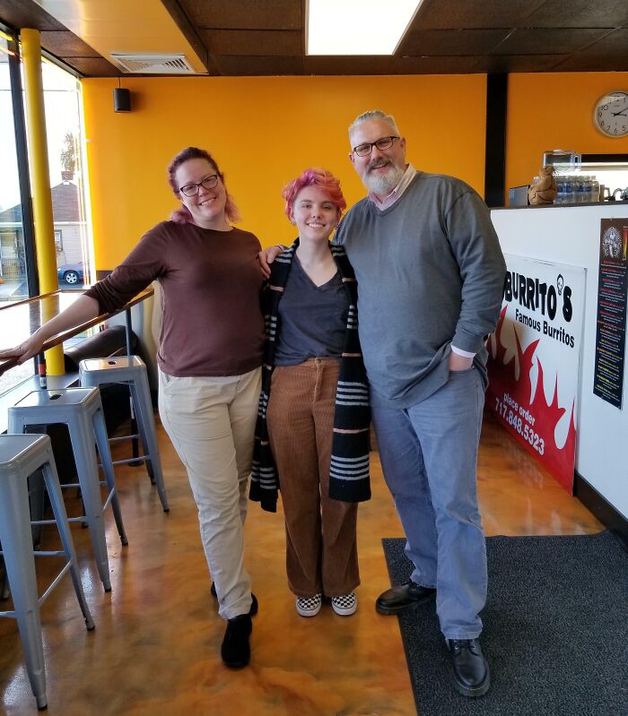 A joyful family, parents and child, smiling together in a restaurant, embodying wholesome adoption stories.