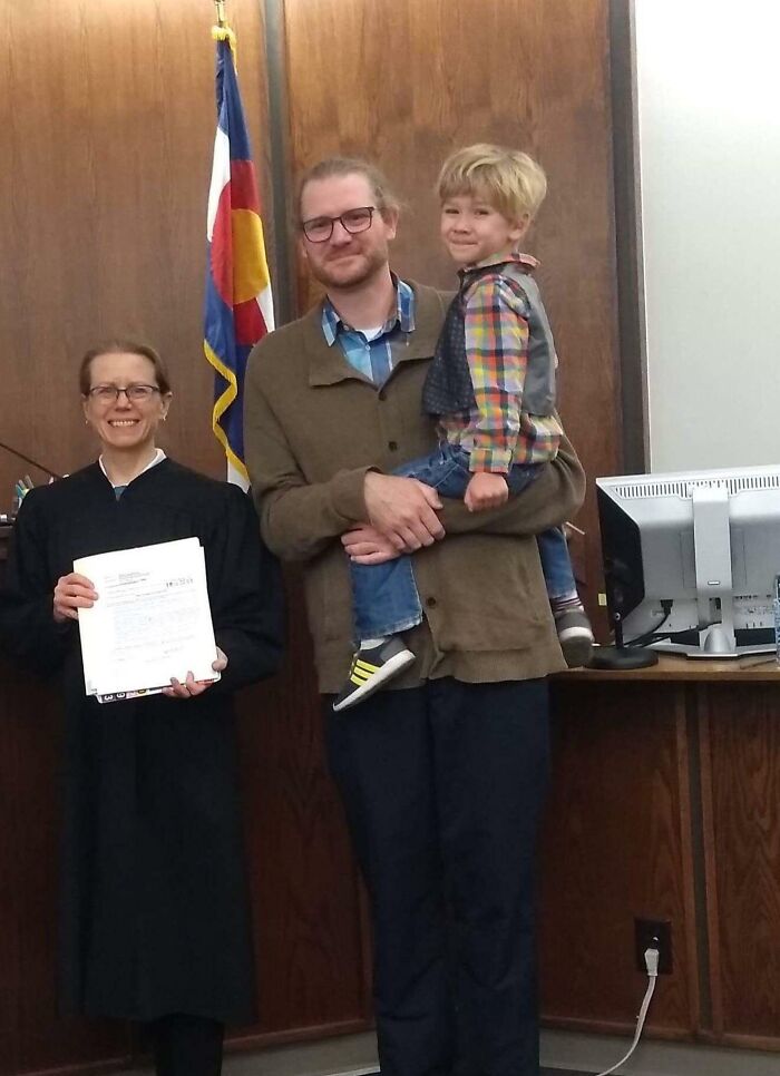 A judge, smiling father, and child at an adoption ceremony highlighting wholesome adoption stories.